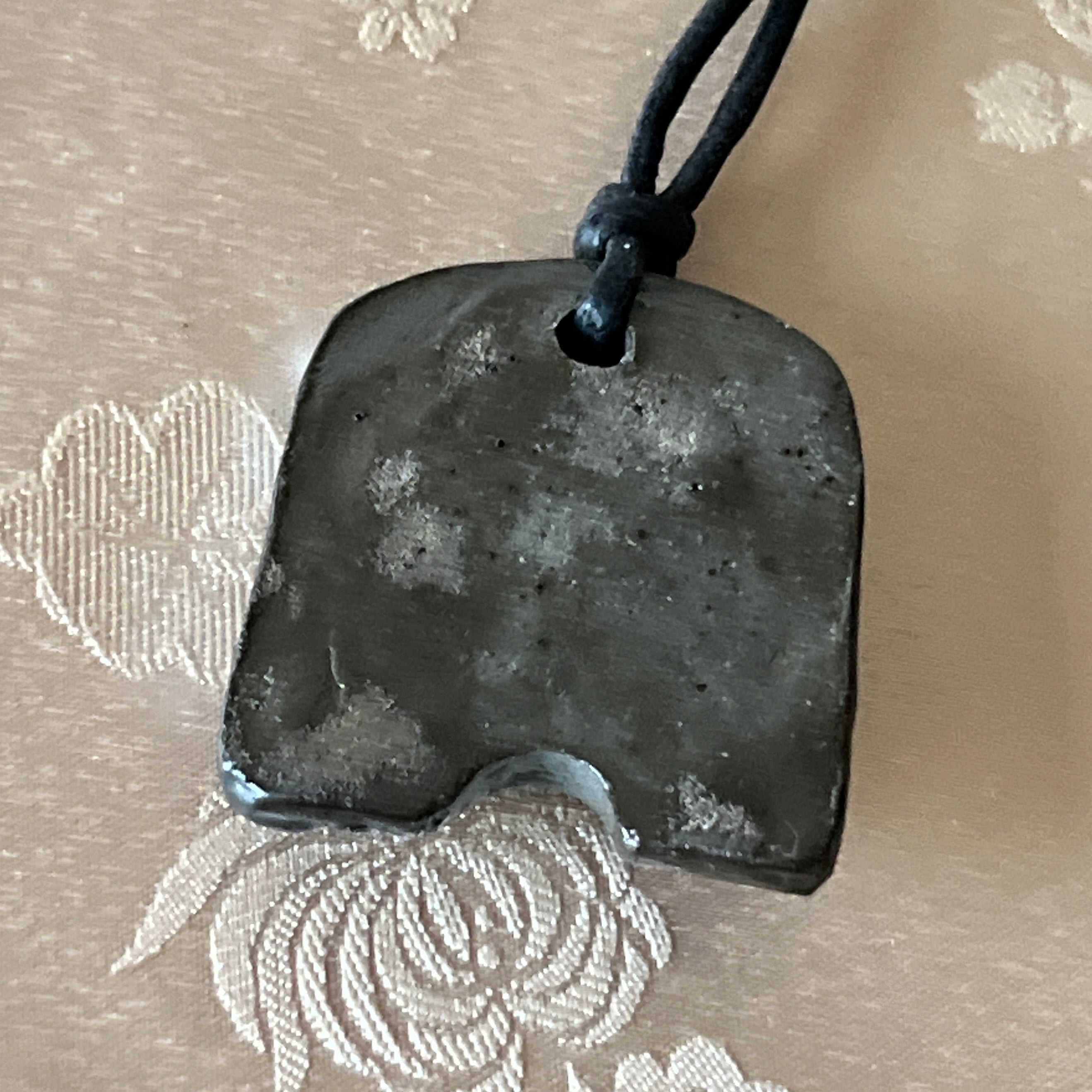Back view of a Korean Silla earthenware Gwimyeonwa pendant necklace showing the dark fired clay surface
