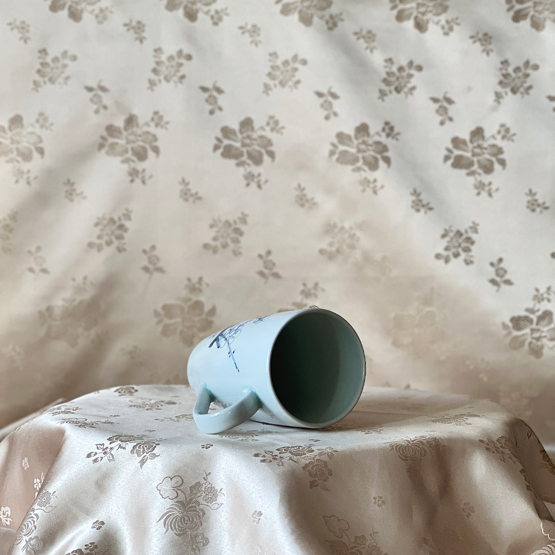 Korean white porcelain mug with blue plum blossom motif, shown on its side with the open rim visible