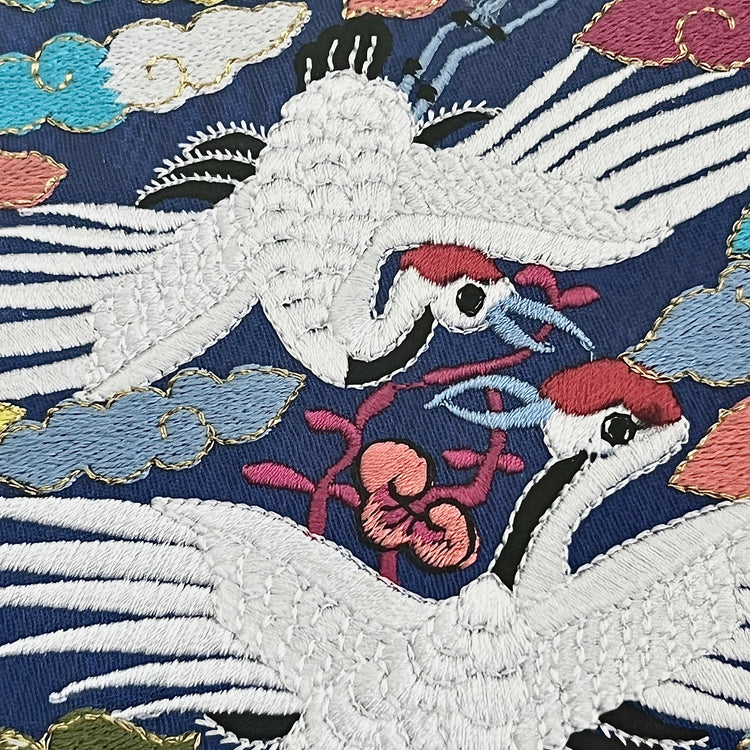 Embroidered design of cranes and flowers on a dark blue background