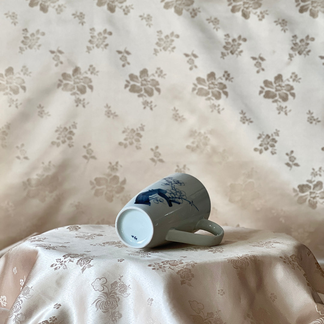 Korean white porcelain mug with hand-painted blue plum blossom design shown lying on its side