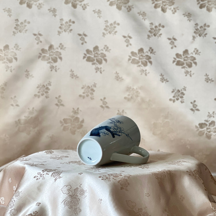Korean white porcelain mug with hand-painted blue plum blossom design shown lying on its side