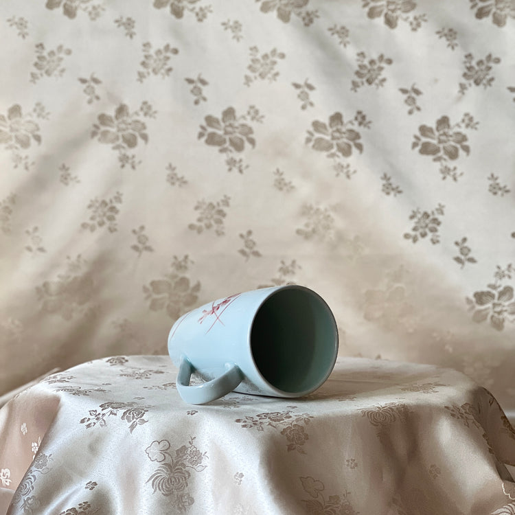 Korean white porcelain mug with red shrimp motif shown lying on its side with the open rim visible