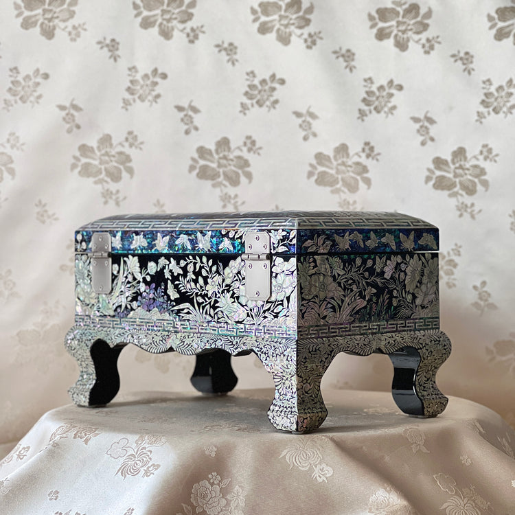 Side view of a Korean mother-of-pearl jewelry box showing black lacquer, floral inlay, and decorative feet