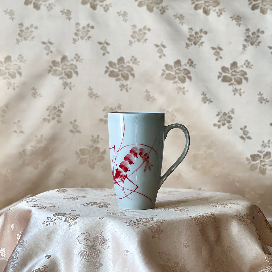 Korean white porcelain mug with red shrimp motif shown upright on soft floral fabric