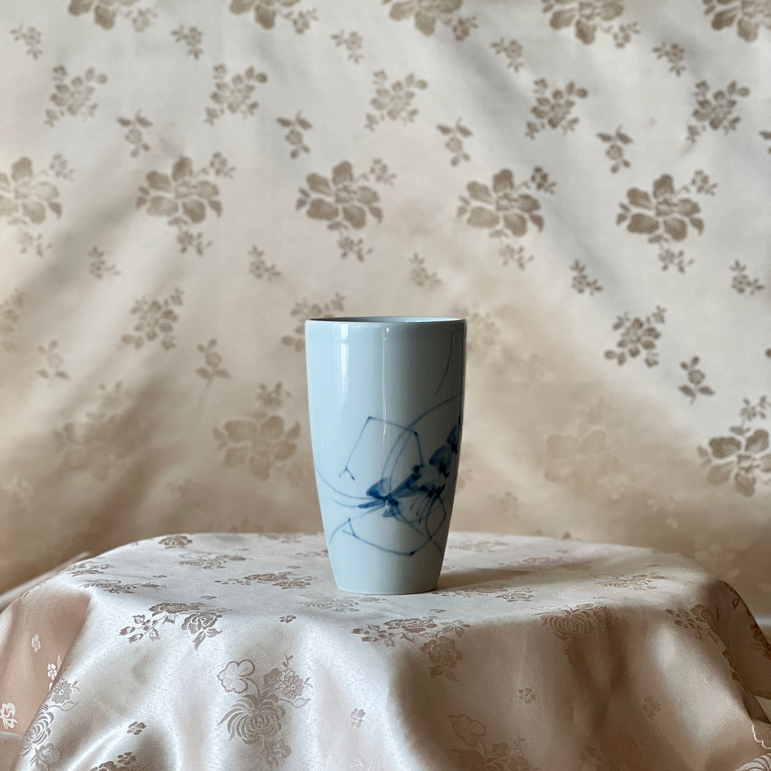 Korean white porcelain mug with blue shrimp motif shown upright on floral fabric