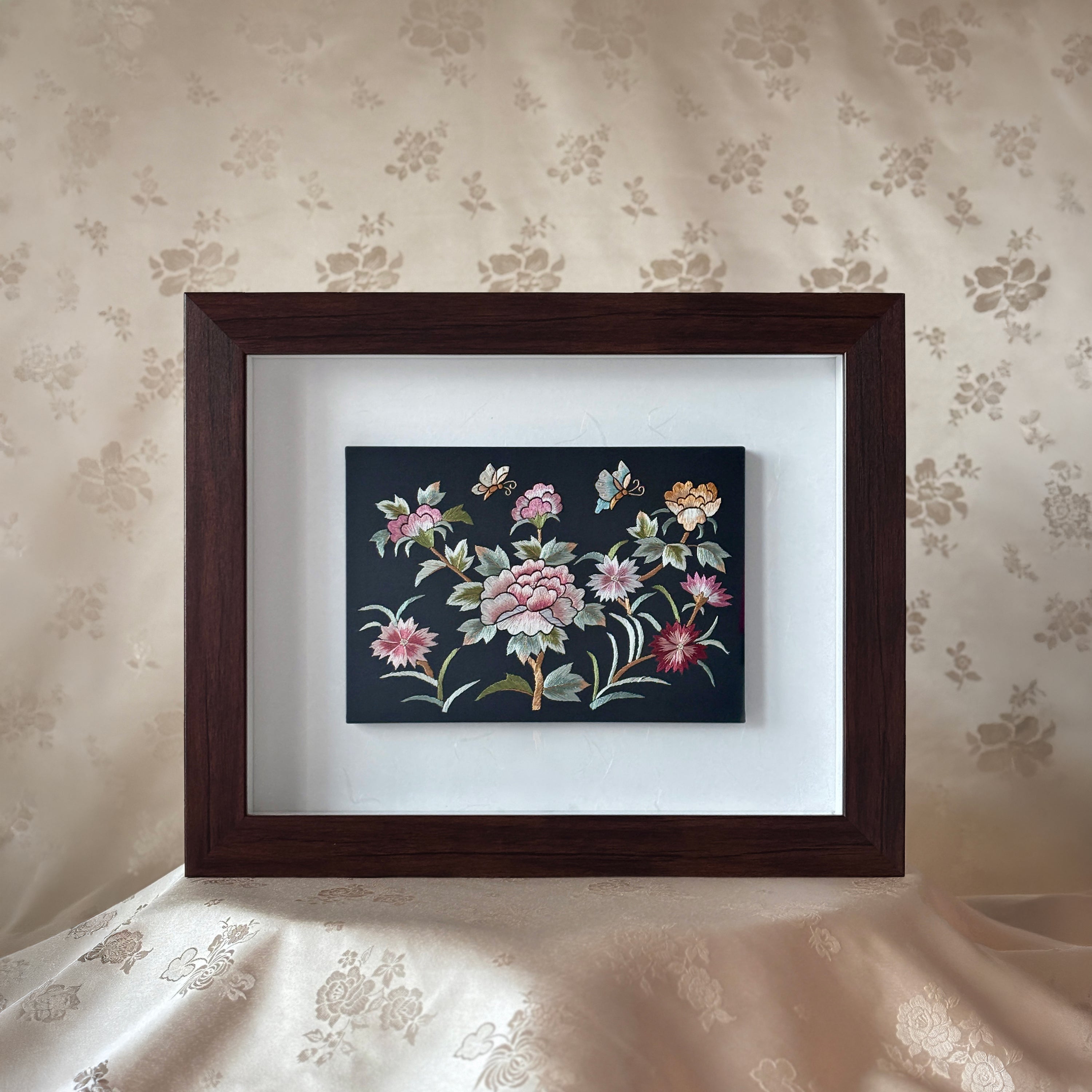 Framed floral embroidery on a floral wallpapered wall
