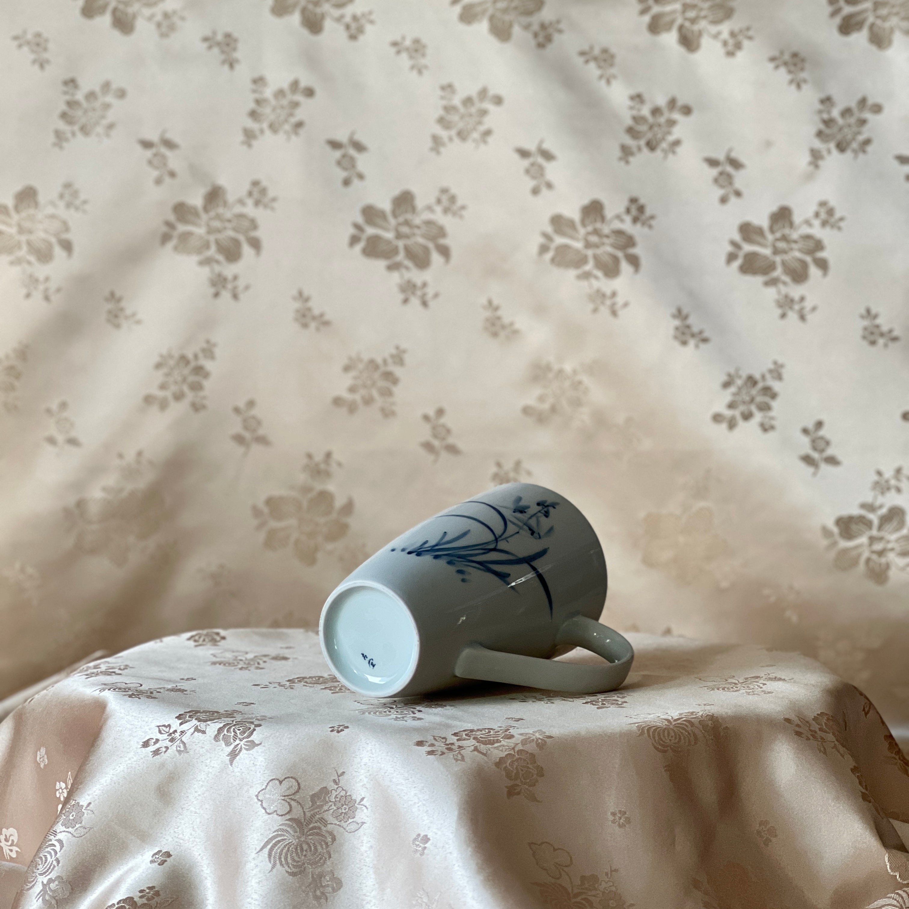 Korean white porcelain mug with blue orchid motif shown lying on its side