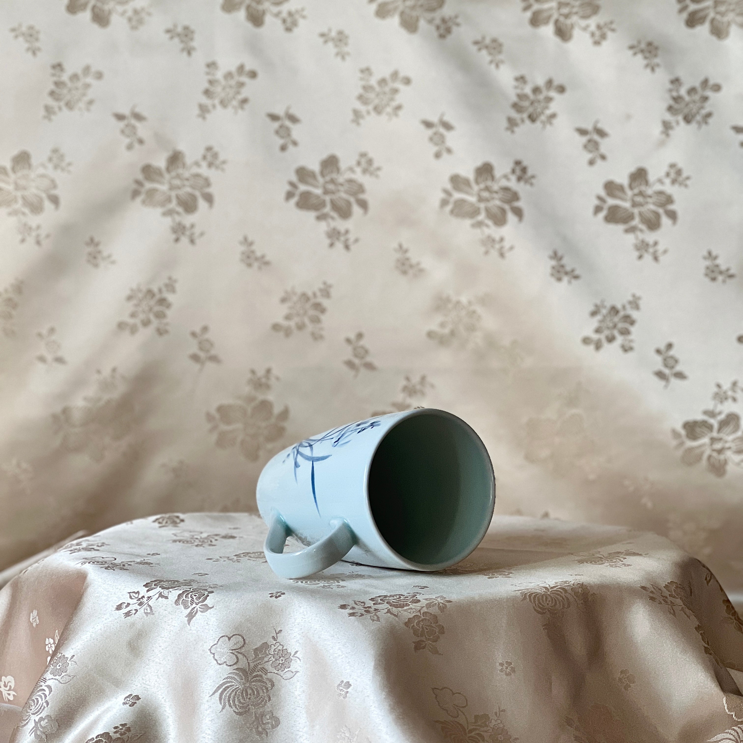 Korean white porcelain mug with blue orchid motif, shown on its side with the open rim visible