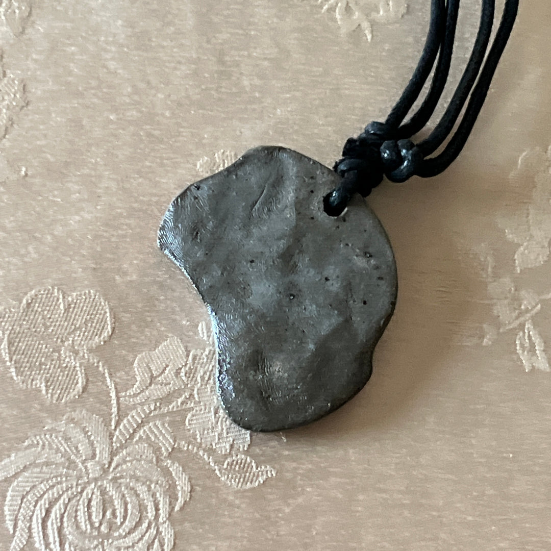 Back view of a Korean Silla earthenware human-face Sumaksae pendant showing the fired clay texture