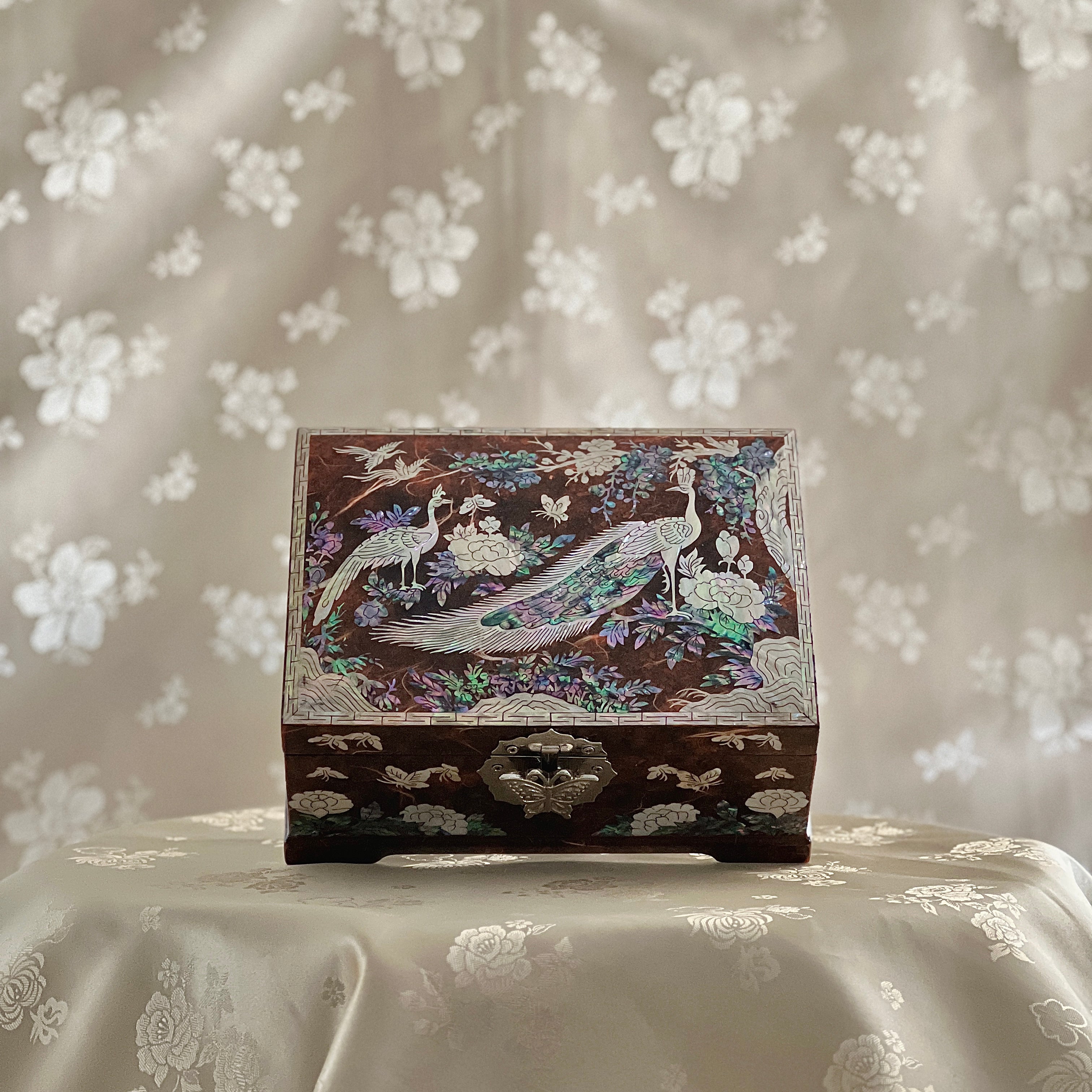 Decorative wooden box with peacock design on a floral-patterned fabric background. Korean art
