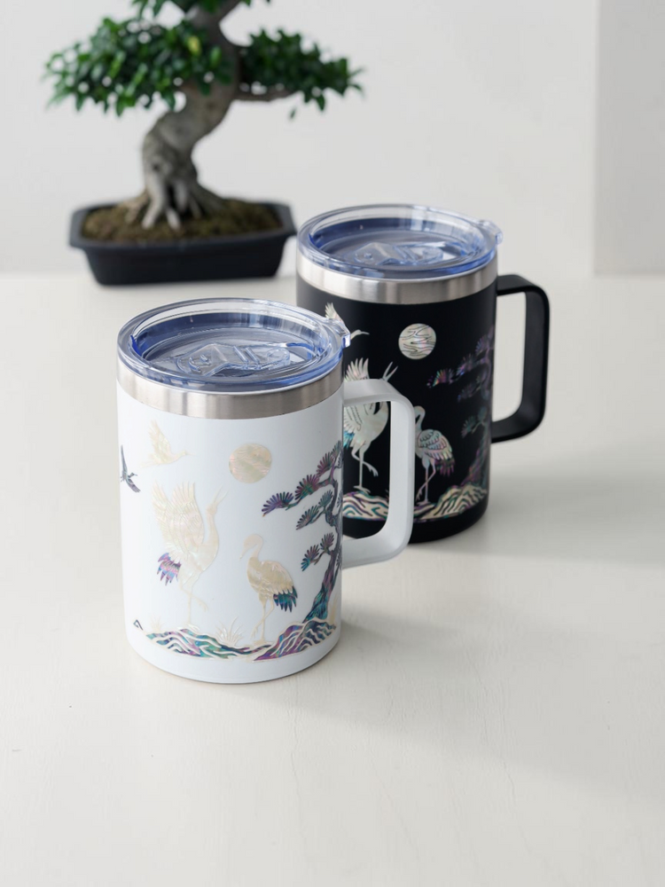 Black and white mother of pearl crane mugs displayed together with a bonsai tree on a light surface