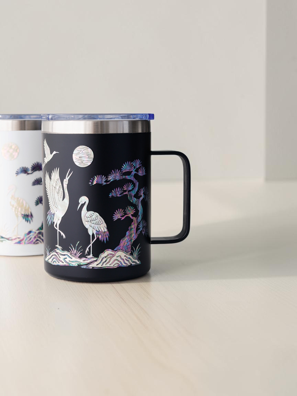 White and black Korean mother of pearl mugs side by side, showing both color options with handles