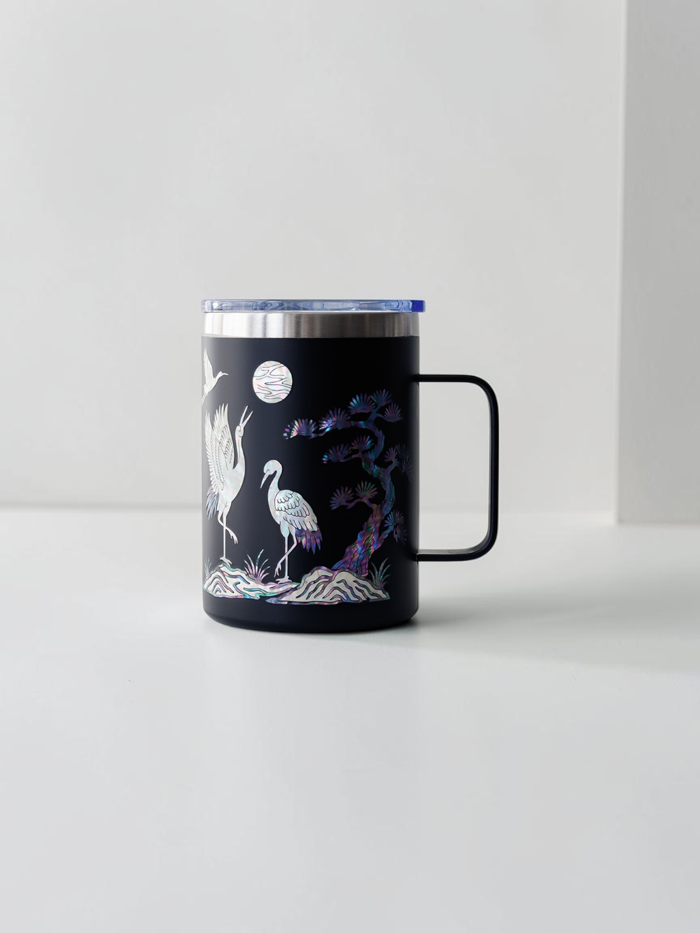 Black stainless mug with handle, mother of pearl cranes flying under a full moon with an inlaid pine tree
