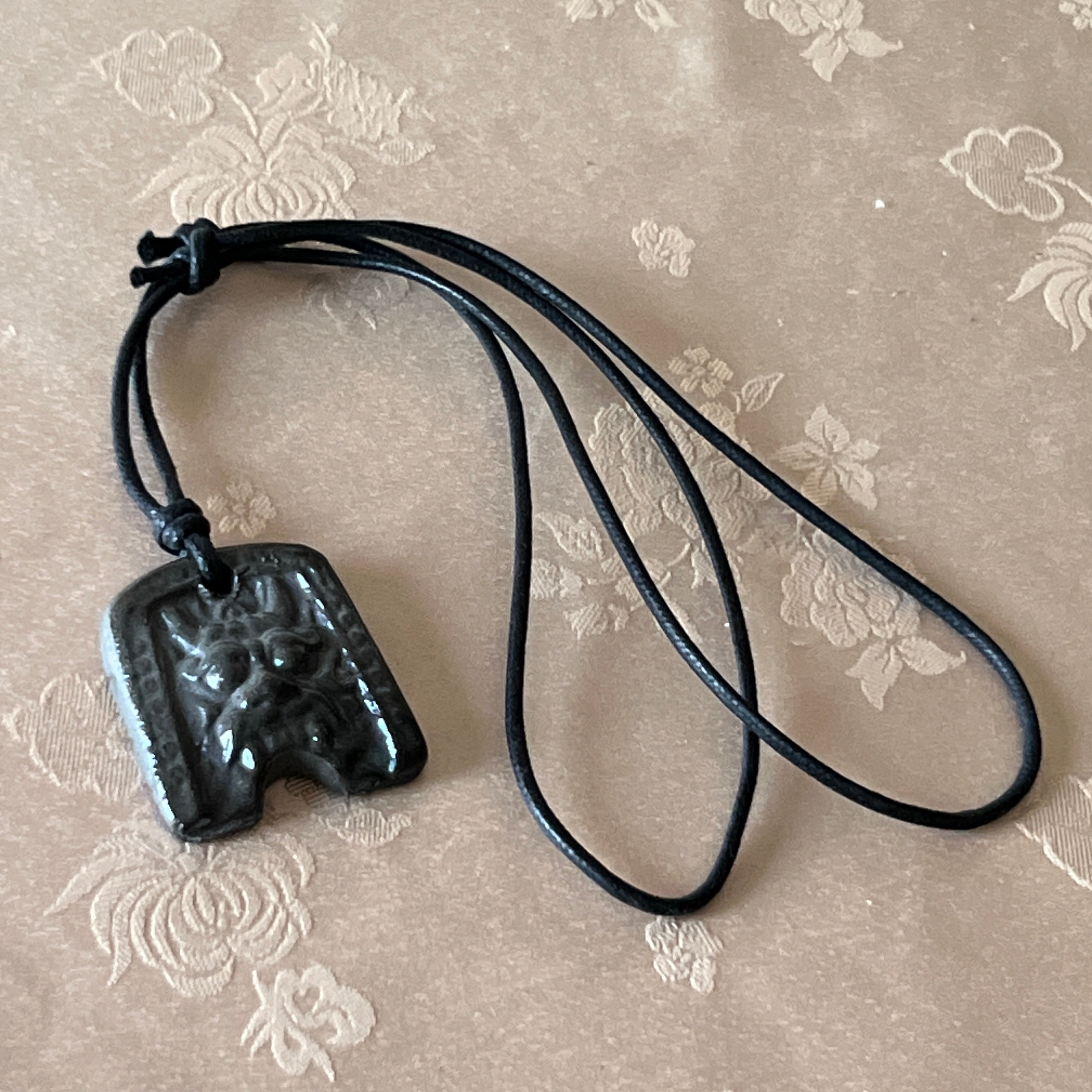 Korean Silla earthenware Gwimyeonwa demon-face pendant with protective mask motif and black cord