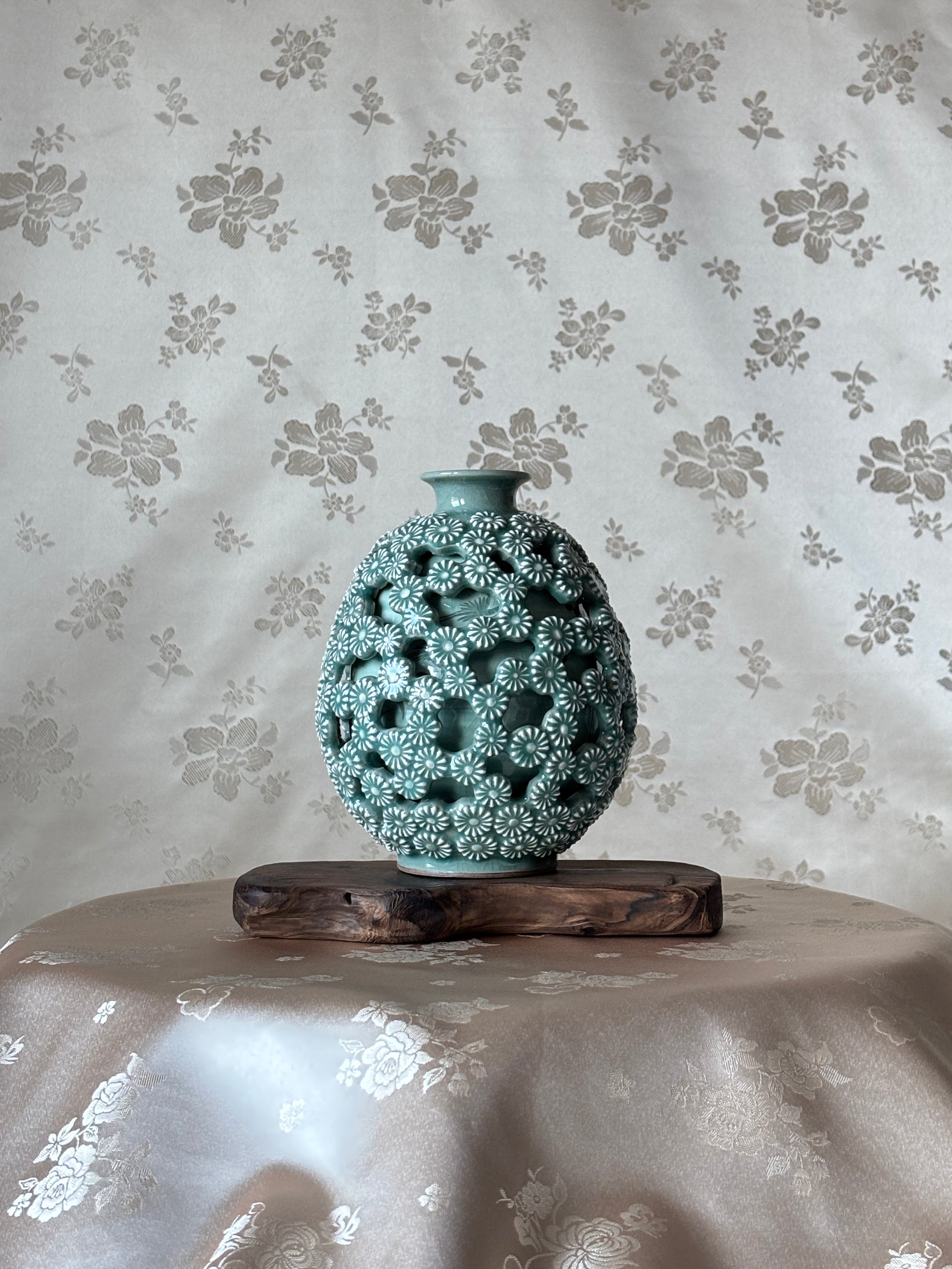 Decorative vase with intricate design on a floral-patterned celadon background