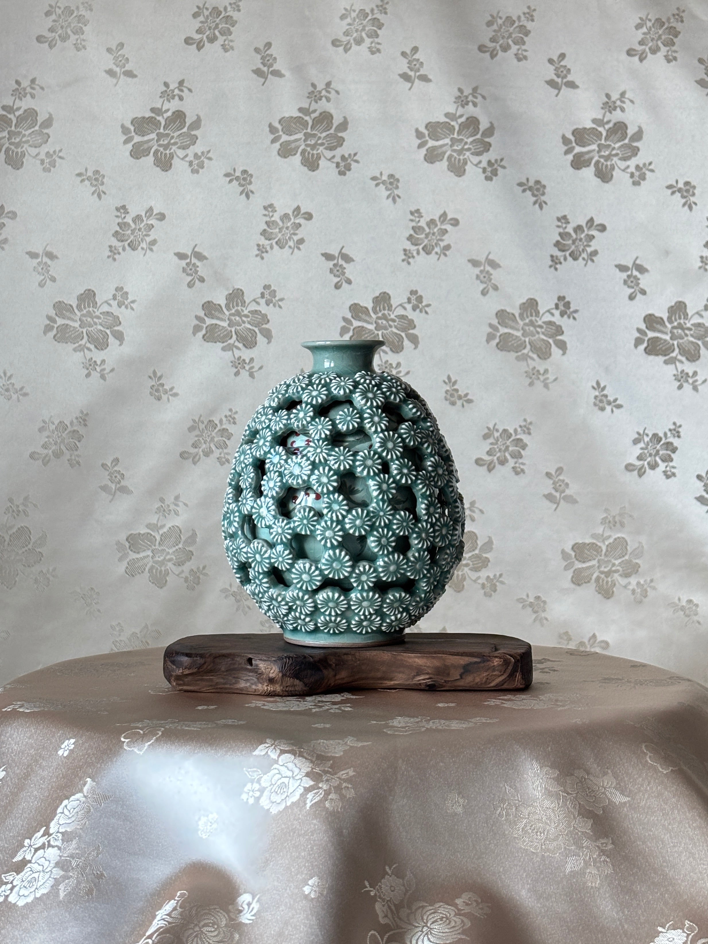 Decorative vase with intricate design on a floral-patterned celadon background