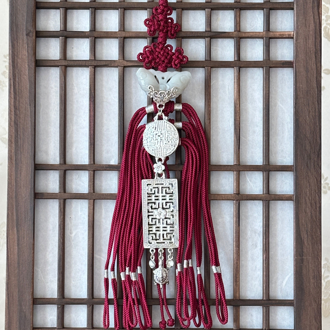 Decorative tassel with red strings and silver emblem on a wooden lattice background