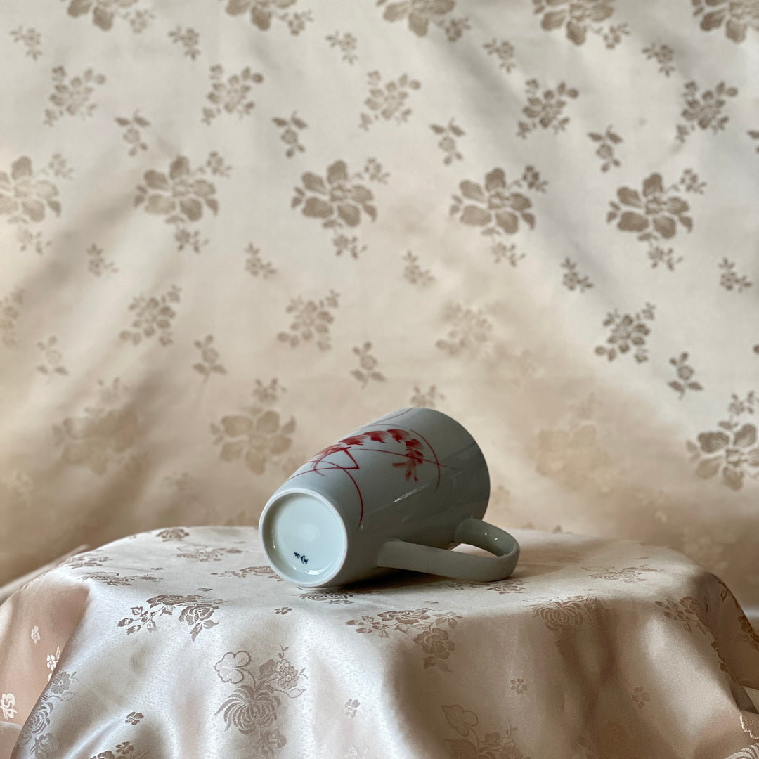Korean white porcelain mug with red shrimp motif shown lying on its side with the foot ring visible