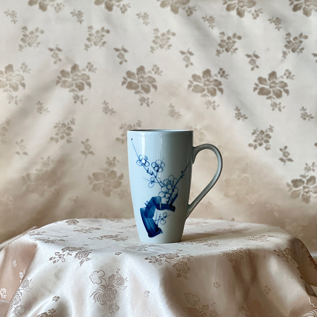 Korean white porcelain mug with blue plum blossom motif shown upright on floral fabric