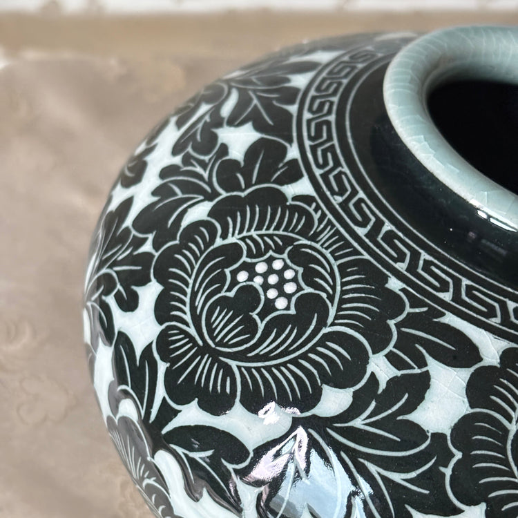 Close-up of a ceramic vase with a glossy black floral pattern on a white glaze, showing part of the dark interior and a light blue-green rim.