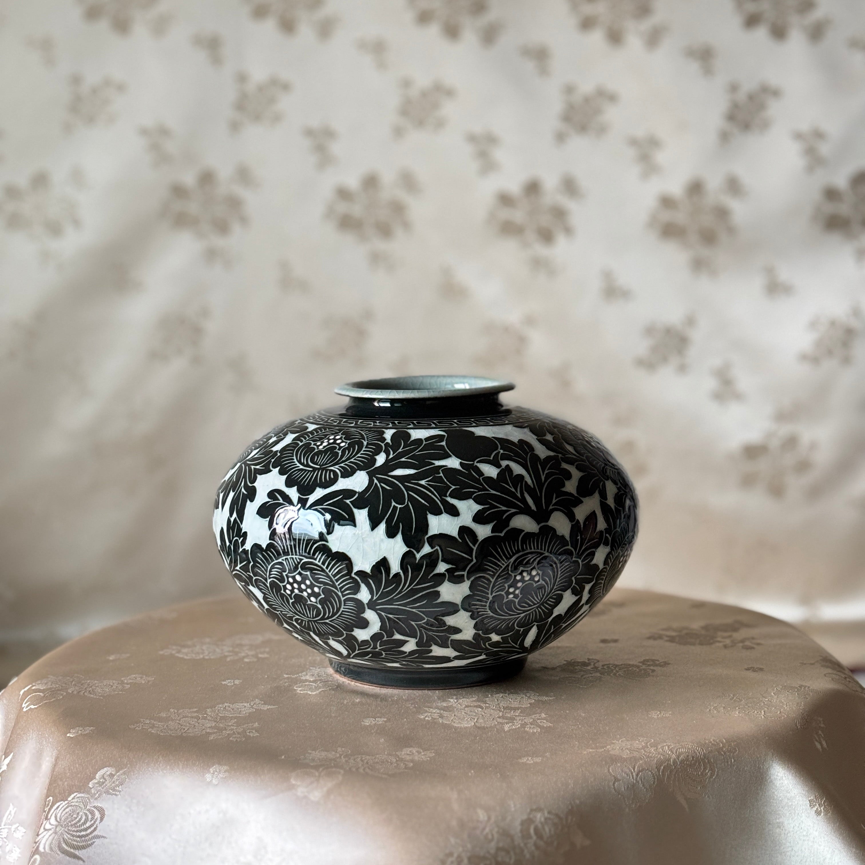 A small round ceramic vase with a black floral pattern on a celadon glaze, korean pottery