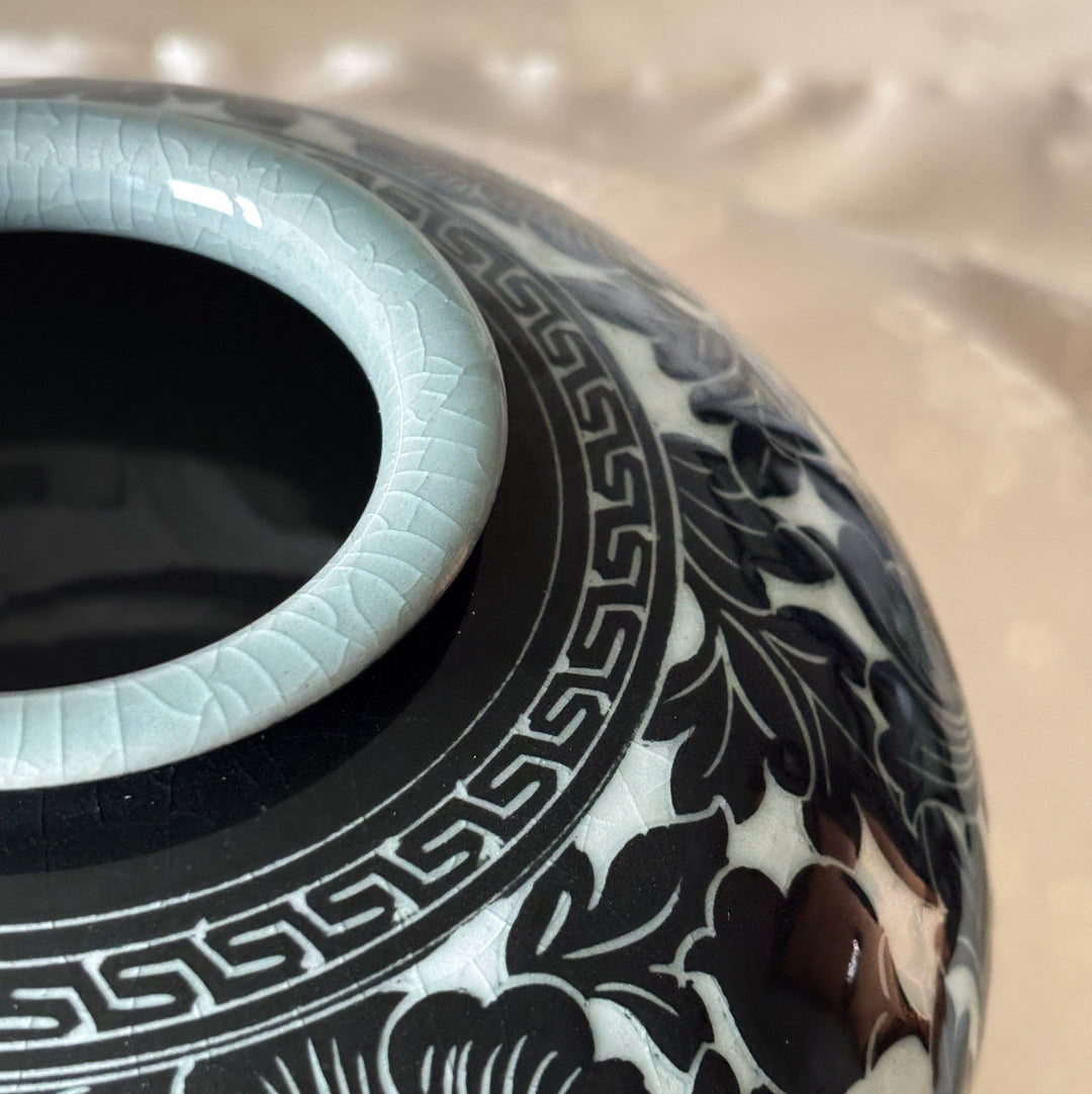 Close-up of a ceramic vase with a glossy black floral pattern on a white base, featuring a pale celadon rim