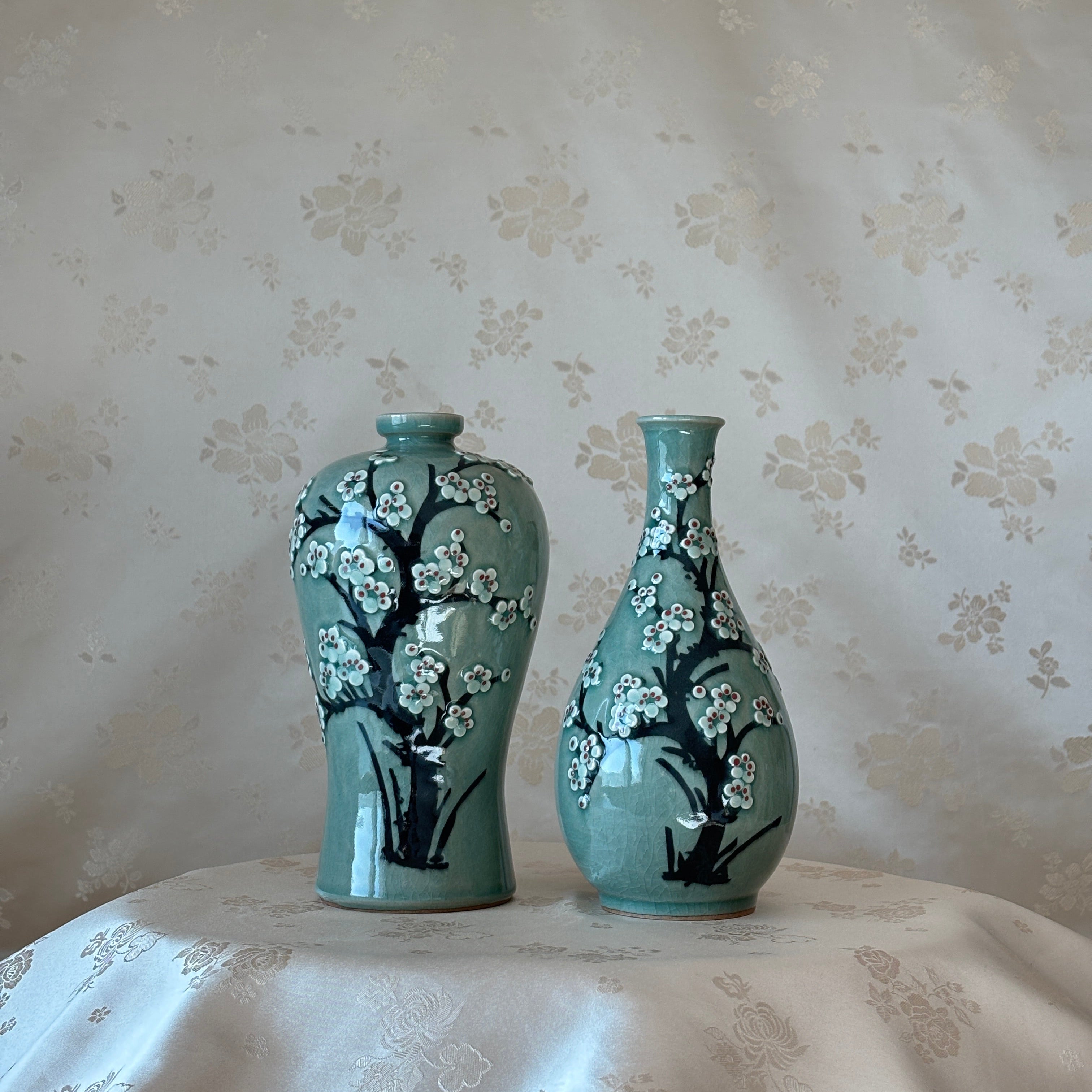 Two turquoise vases with black floral patterns on a floral-patterned fabric background