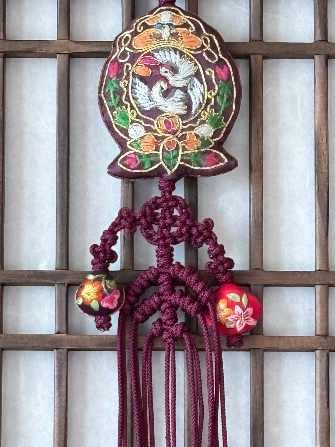 Decorative hanging norigaewith floral patterns and tassels against a wooden lattice background