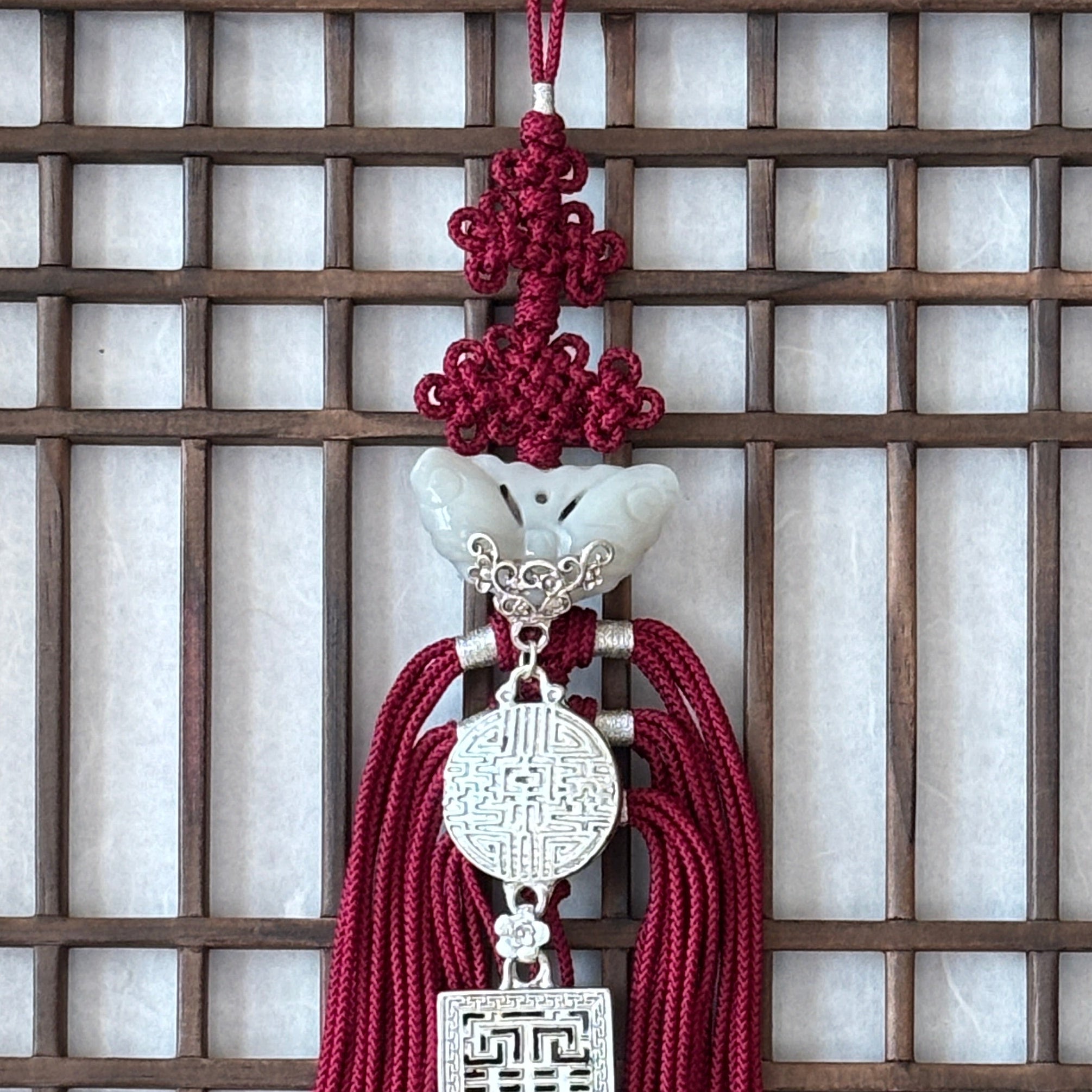 Decorative tassel Korean norigae with red strings and silver emblem on a wooden lattice background