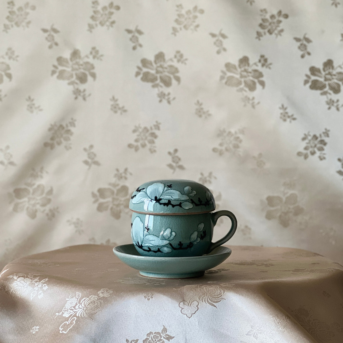 Tea cup and saucer with floral design on a floral-patterned tablecloth