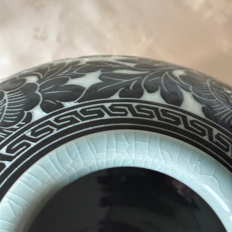 Close-up of a ceramic vase or bowl with a glossy black floral pattern on a white base, showing a pale celadon rim and dark interior.