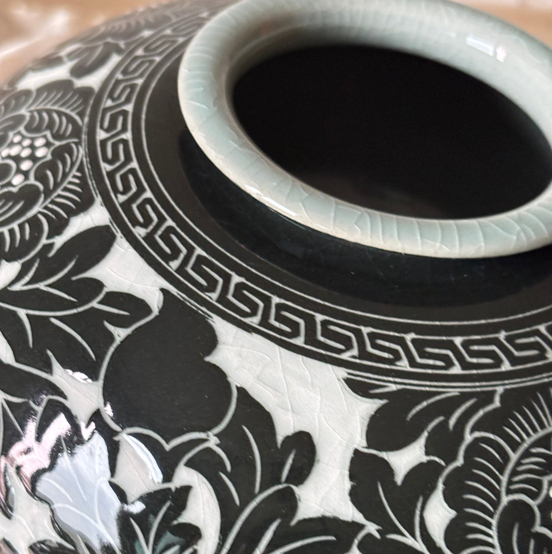 Close-up of a ceramic vase with a glossy black and white floral pattern, featuring a Korean peony motif around the neck and a pale celadon glaze on the interior.