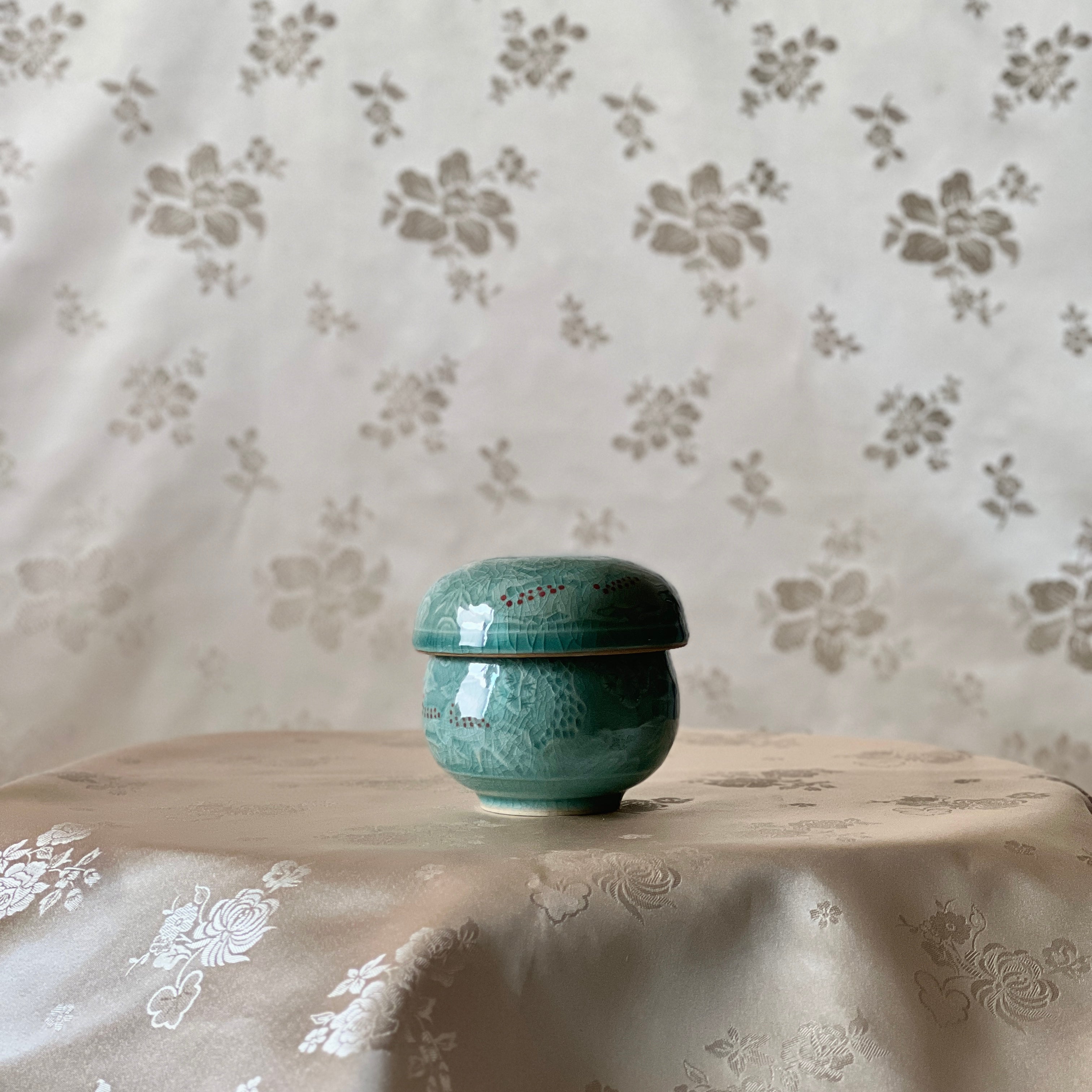 Celadon ceramic cup on a floral-patterned tablecloth