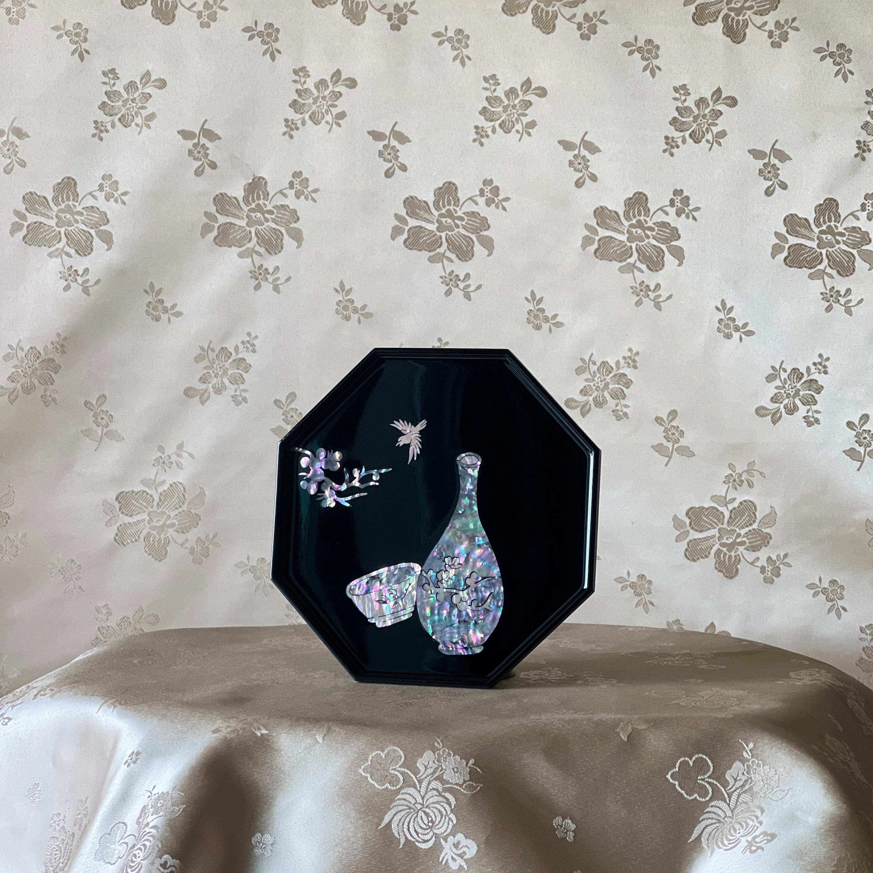Korean mother of pearl octagonal tray with vase and cup inlay on black lacquer, angled view on silk fabric.