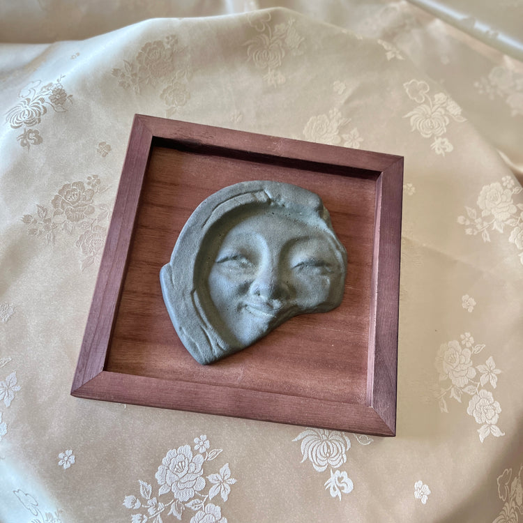 Decorative wall art with a face sculpture in a wooden frame on a floral fabric background