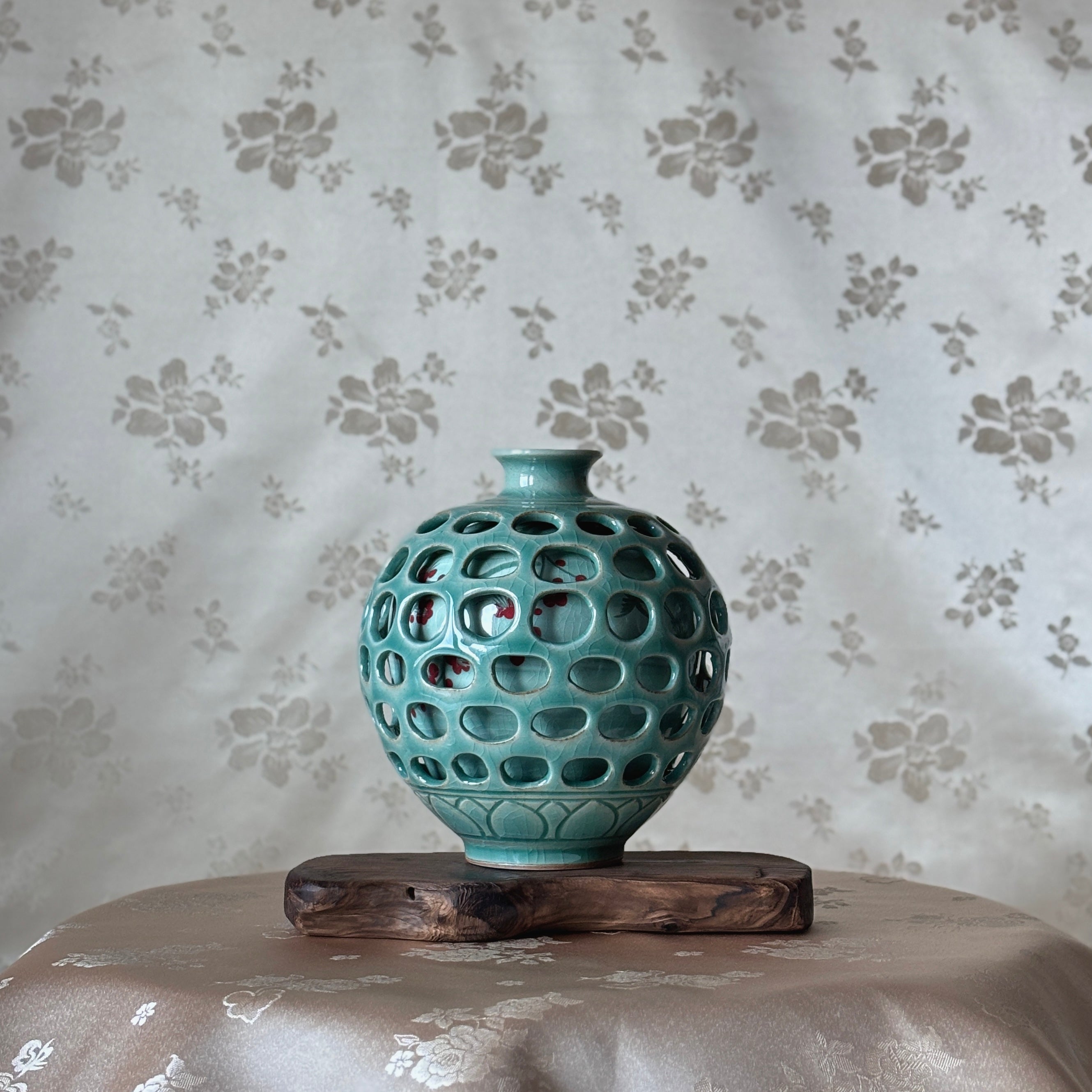  ceramic vase with a textured surface on a wooden stand against a floral-patterned wall.