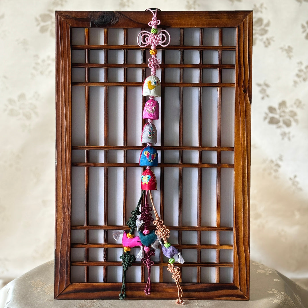 A colorful traditional Korean Norigae hanging in a wooden frame, with various embroidered designs and thimble-shaped details.