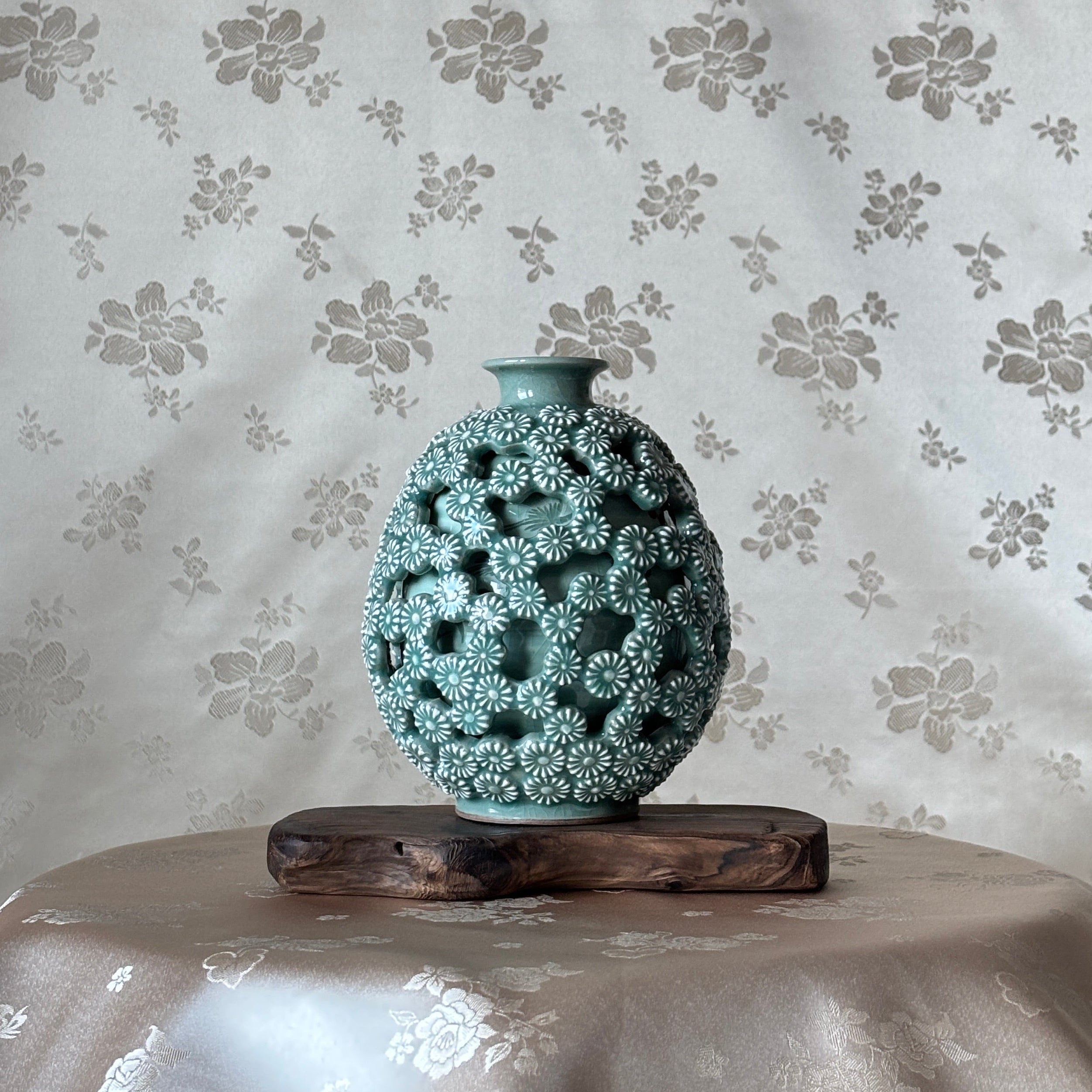 Decorative vase with intricate design on a floral-patterned celadon background