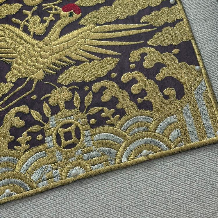 Close-up of an embroidered rug with a crane design on a gray surface.