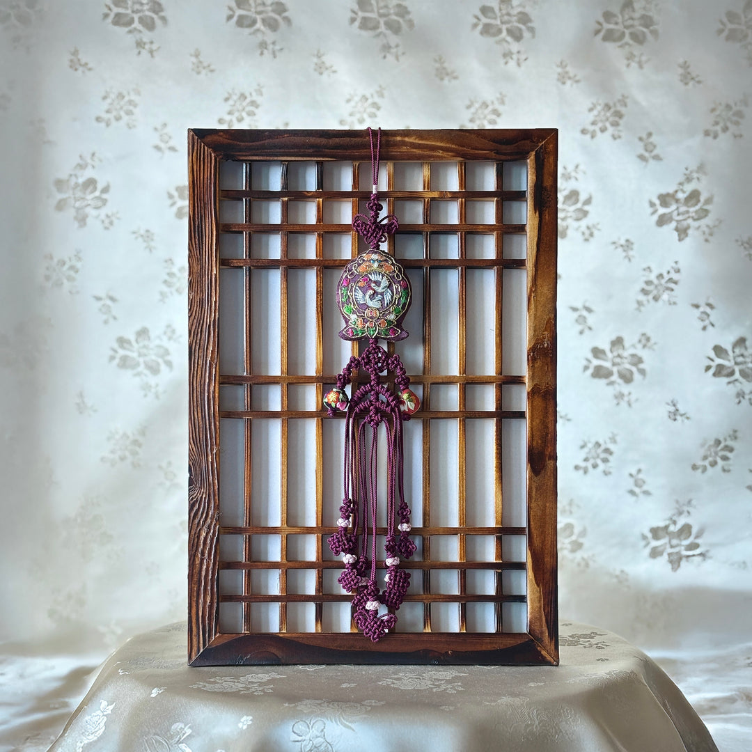 A traditional Korean Norigae featuring embroidery and tassels displayed in a wooden frame against a patterned background.