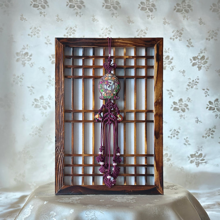 A traditional Korean Norigae featuring embroidery and tassels displayed in a wooden frame against a patterned background.