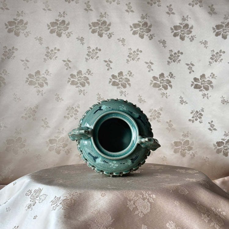 Decorative ceramic vase on a surface with floral-patterned fabric background