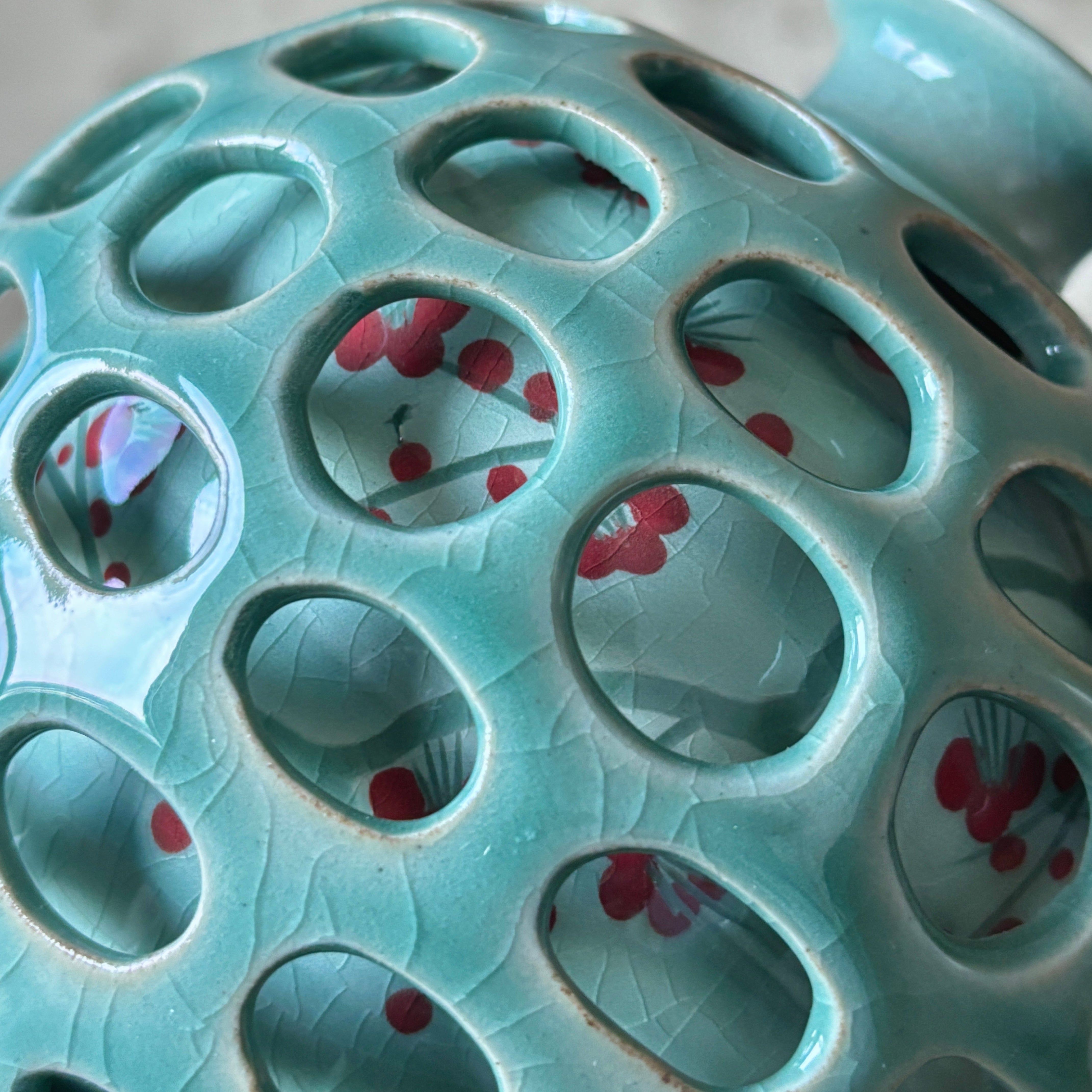 Teal ceramic vase with circular holes and red floral patterns