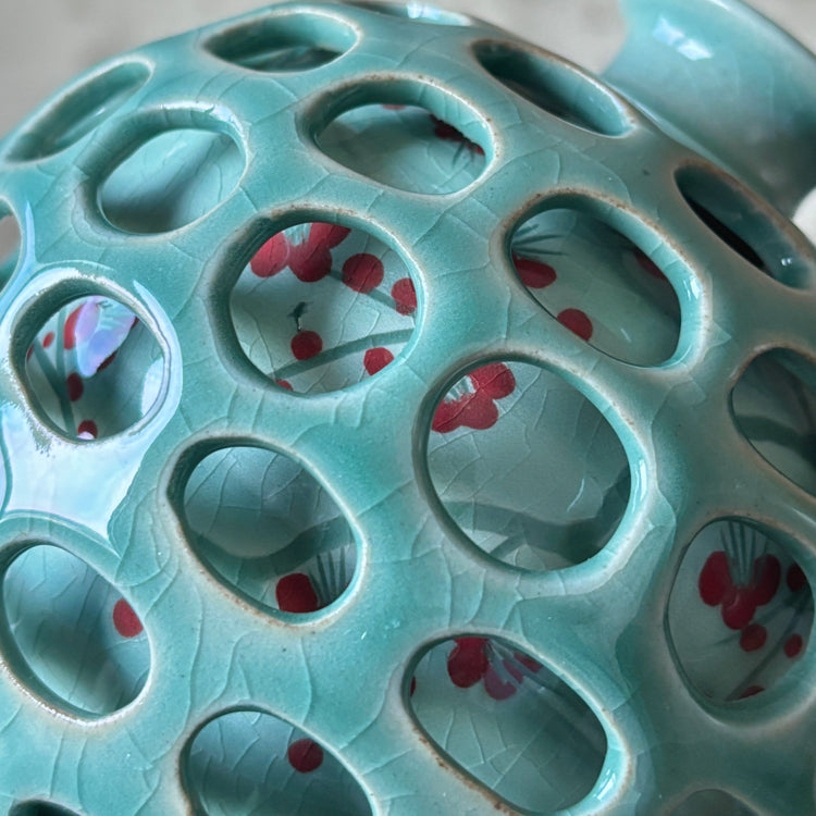 Teal ceramic vase with circular holes and red floral patterns