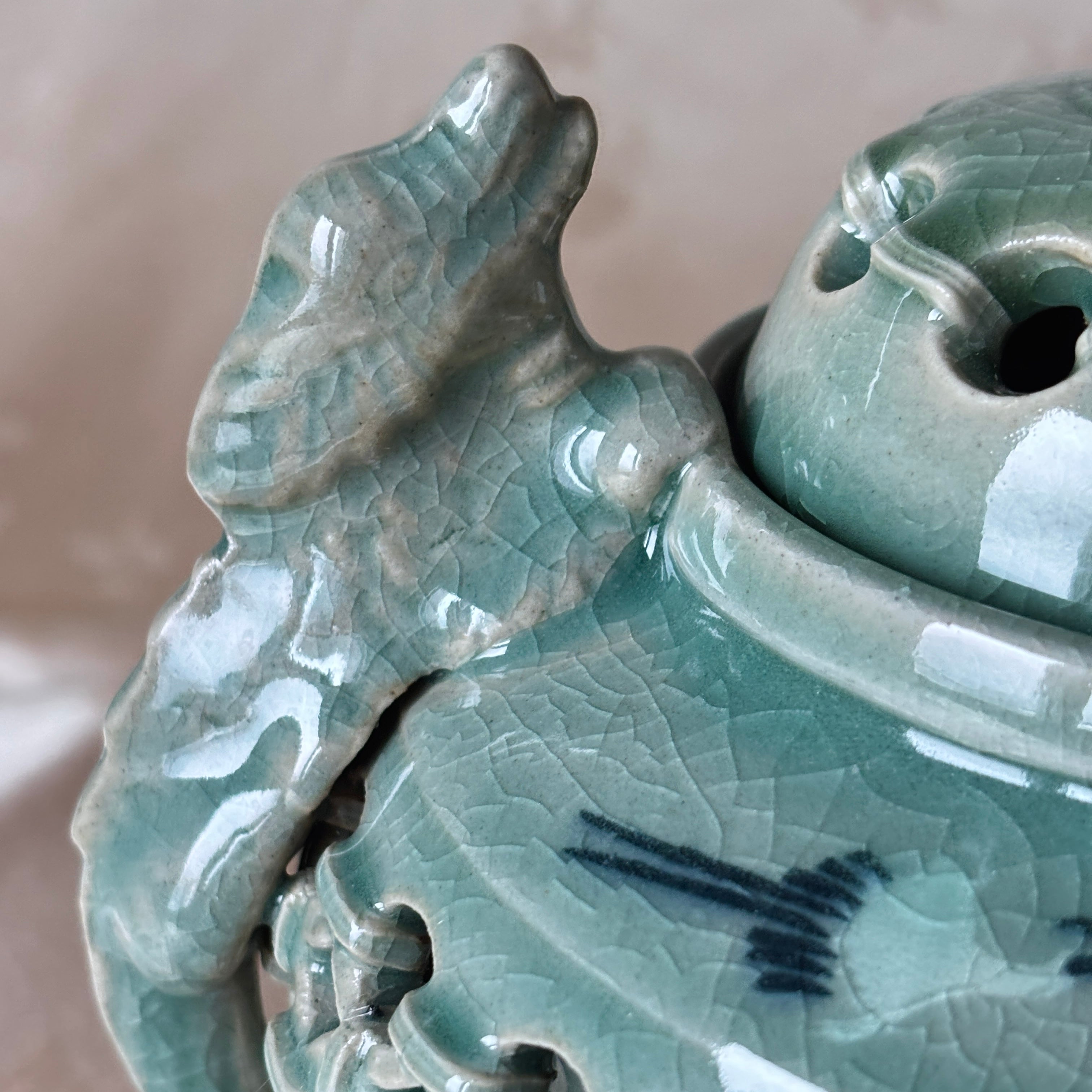 Close-up of a green ceramic vase with dragon design on a beige background