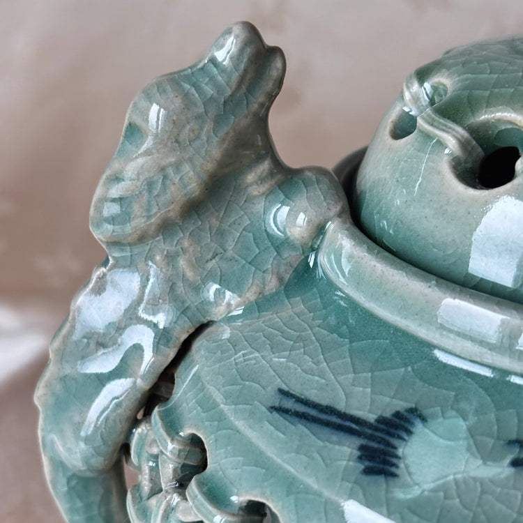 Close-up of a green ceramic vase with dragon design on a beige background