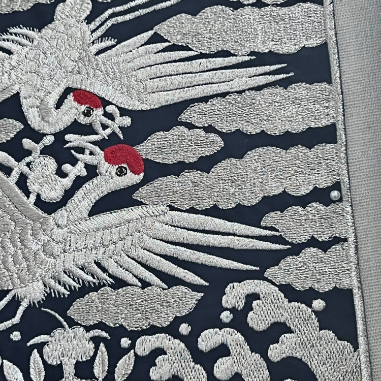 Embroidered design of cranes and clouds on a dark background