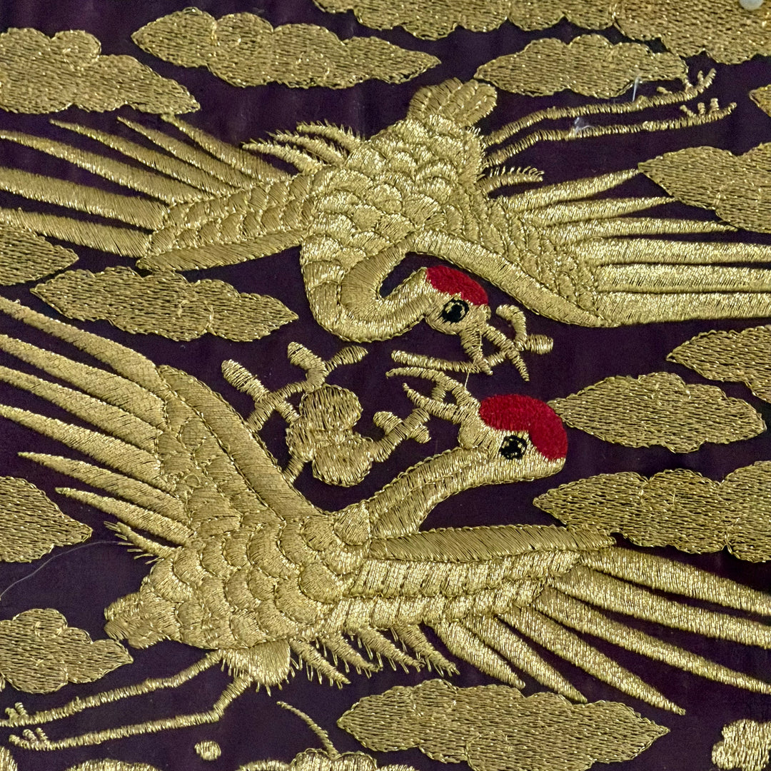 Embroidered design of two cranes on a dark background