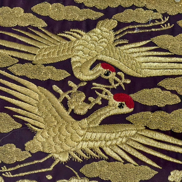 Embroidered design of two cranes on a dark background