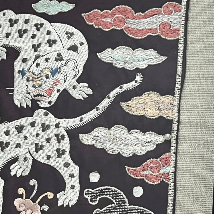 Embroidered design of a tiger or leopard with cloud patterns on a dark background